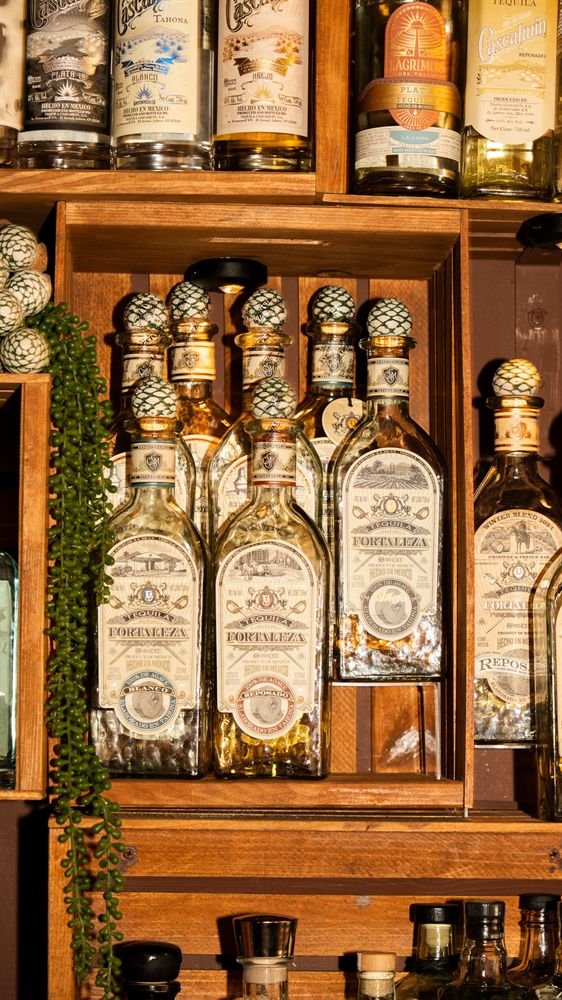 Fortaleza tequila bottles in a lit wooden crate on La Licor's agave and rum back bar