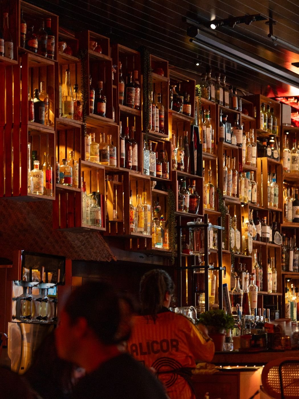 Guests at the bar beneath a wall of glowing bottle crates, the room available for private events